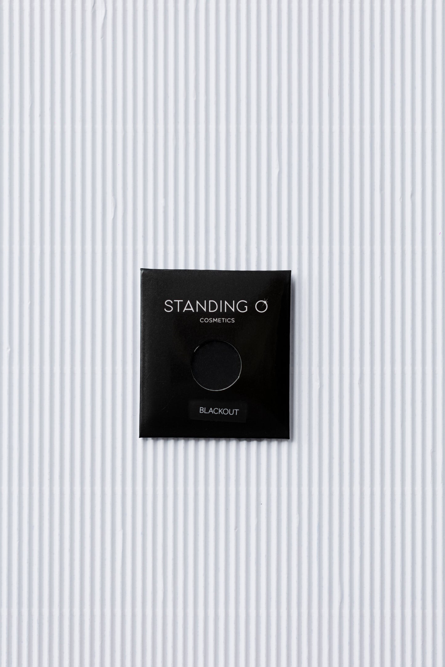 A black single eyeshadow called 'Black Out' by Standing O Cosmetics, showcasing its intense color and smooth texture.