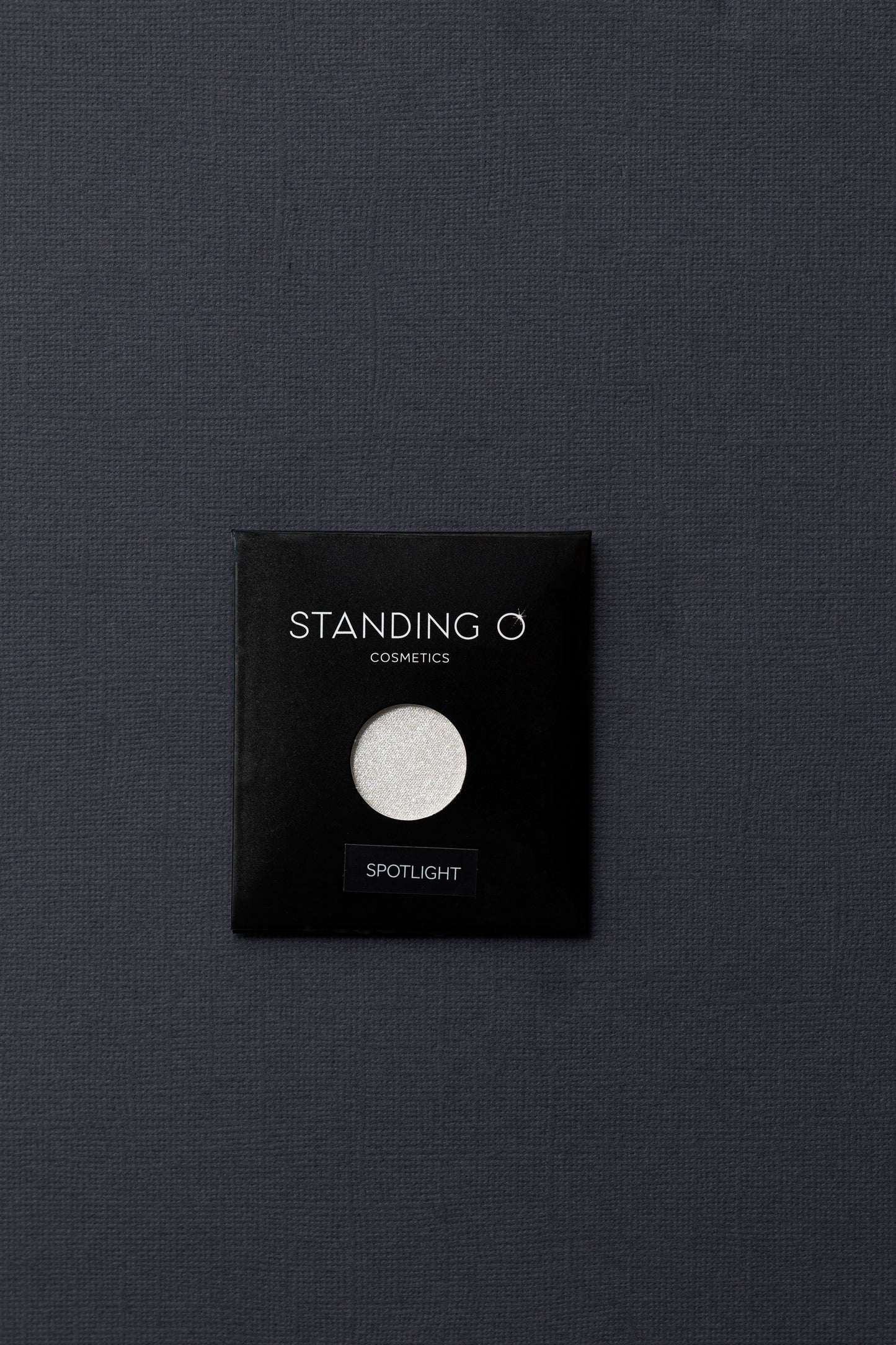 A single eyeshadow called 'Spotlight' by 'Standing O Cosmetics', showcasing its intense silver shimmer and smooth texture.
