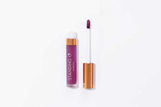 Tube of lipstick with a gold top shown open to showcase the applicator and color: dark purple lipstick.
