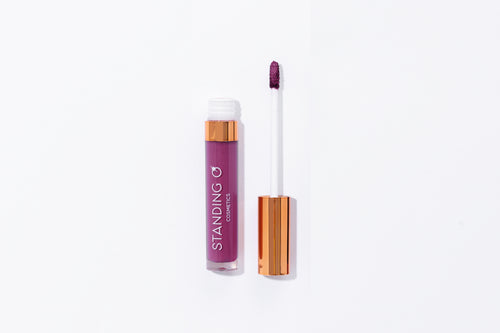 Tube of lipstick with a gold top shown open to showcase the applicator and color: dark purple lipstick.